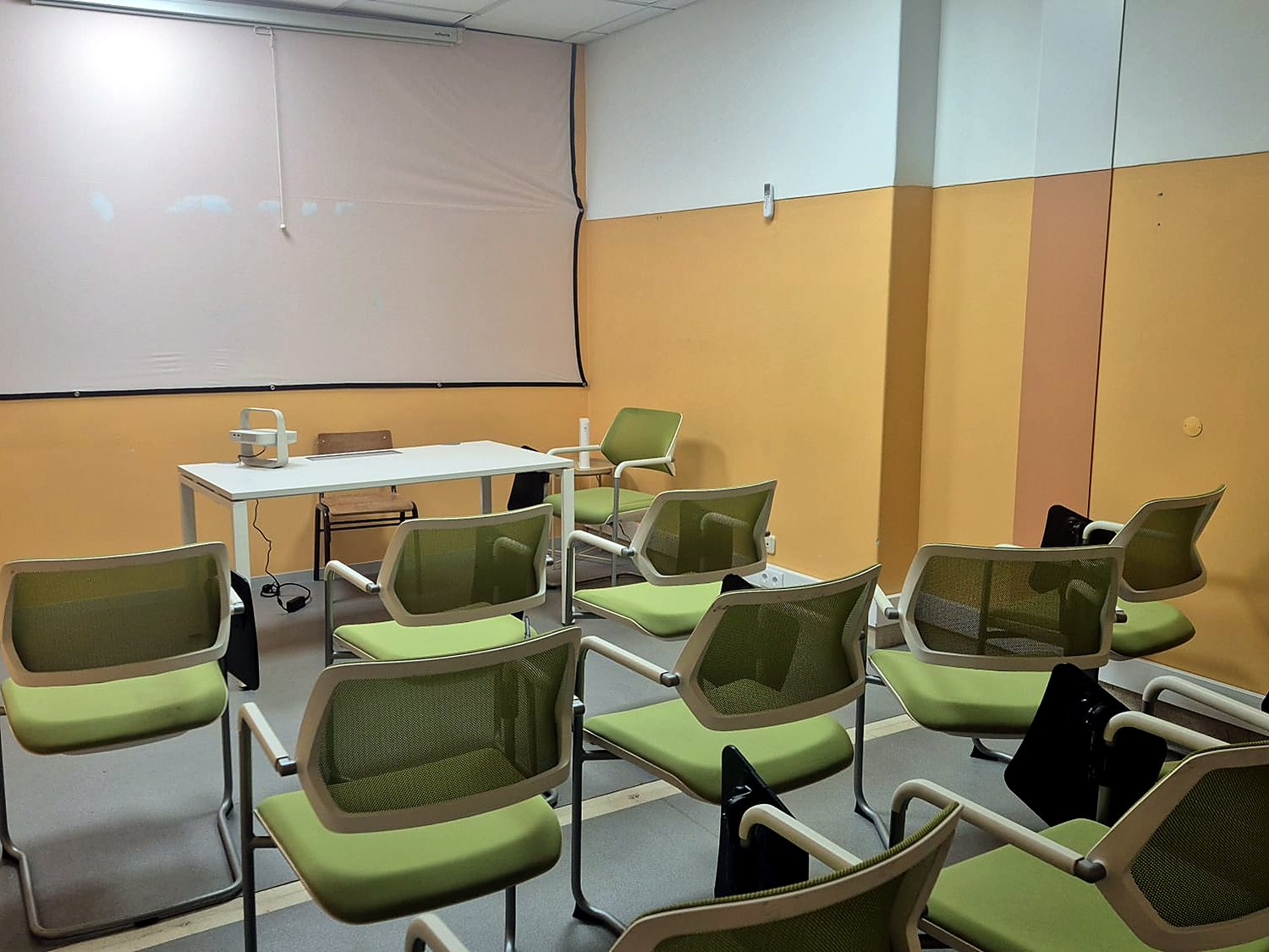 Sala de formação com ecrã de projecção, projector e cadeiras com palmatória